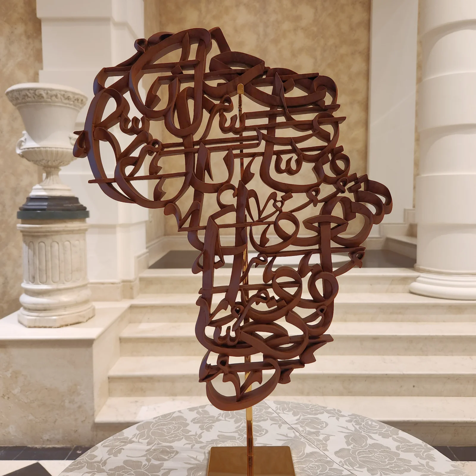 Africa-shaped calligraphic sculpture displayed on a fabric-covered plinth